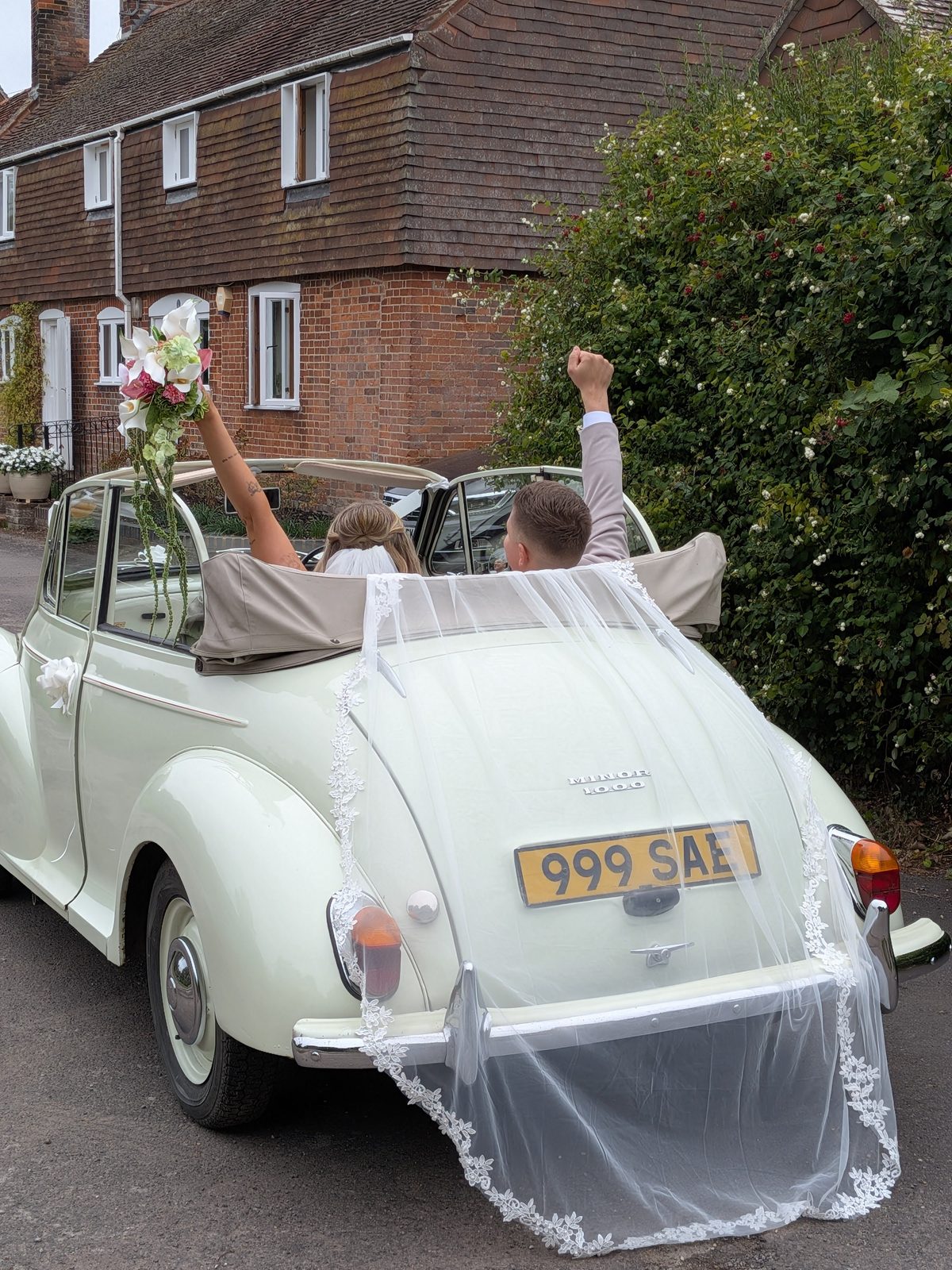 Bride and groom waving from Annie the Morris Minor wedding car, Wiltshire