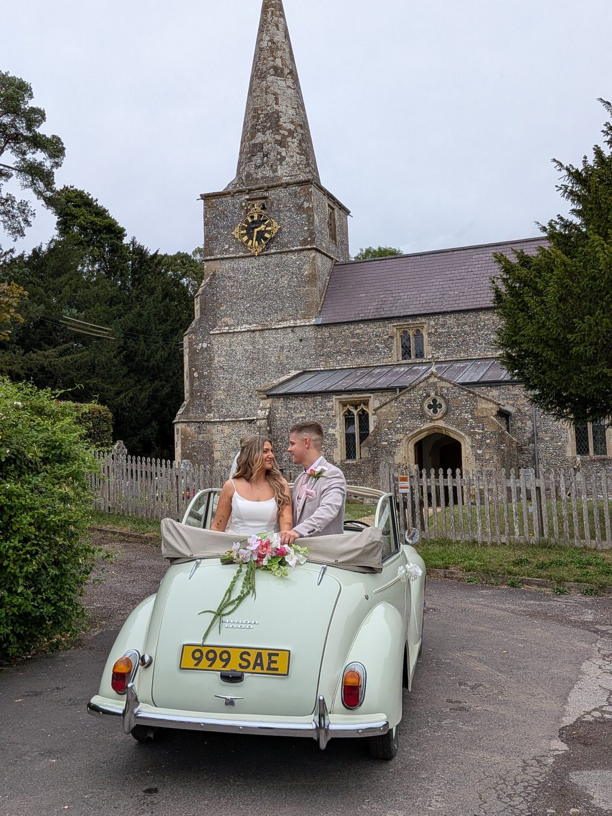Bride and groom by Annie the Morris Minor outside a Wiltshire village church